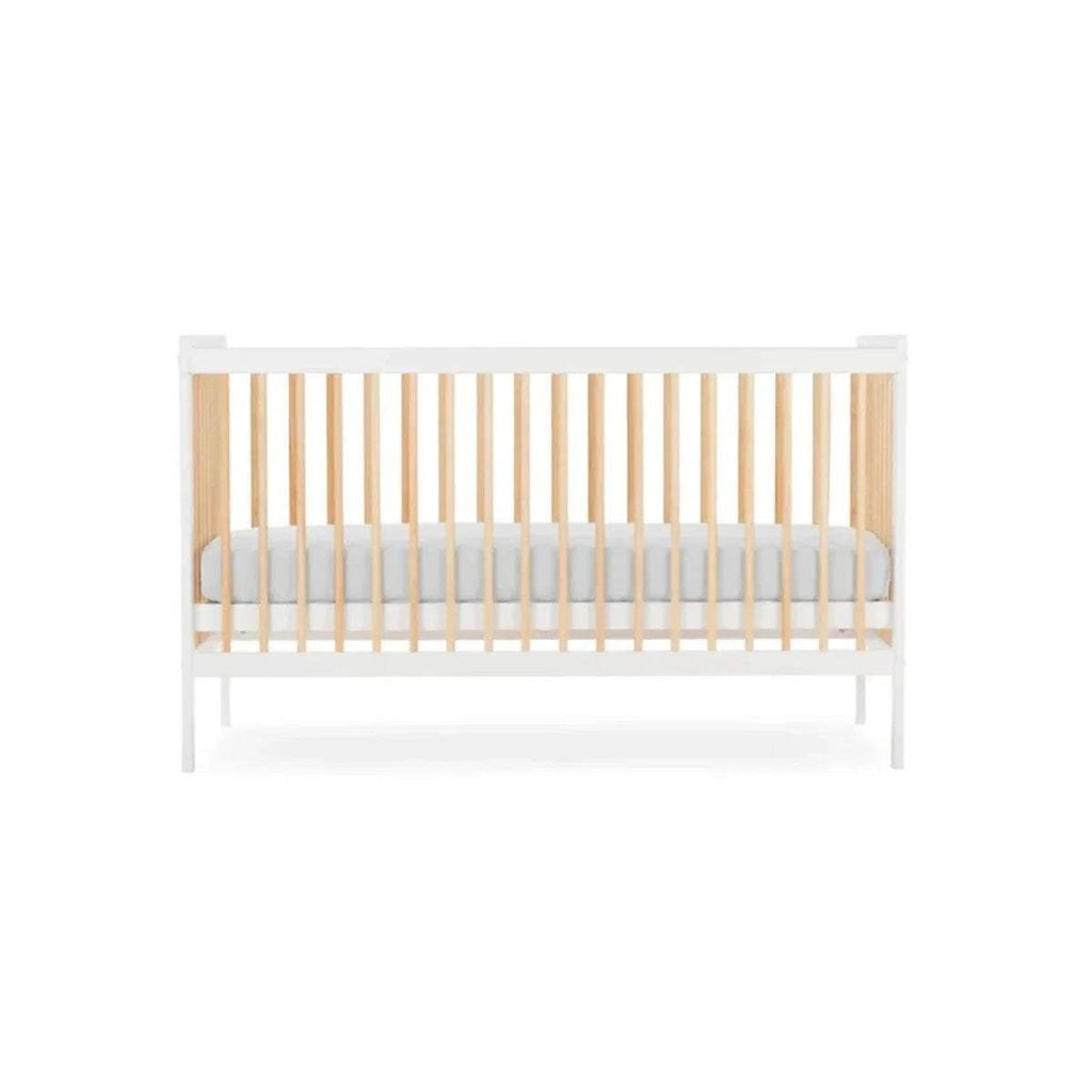 White cot bed with natural slatted rails and light grey mattress insert, angled view.