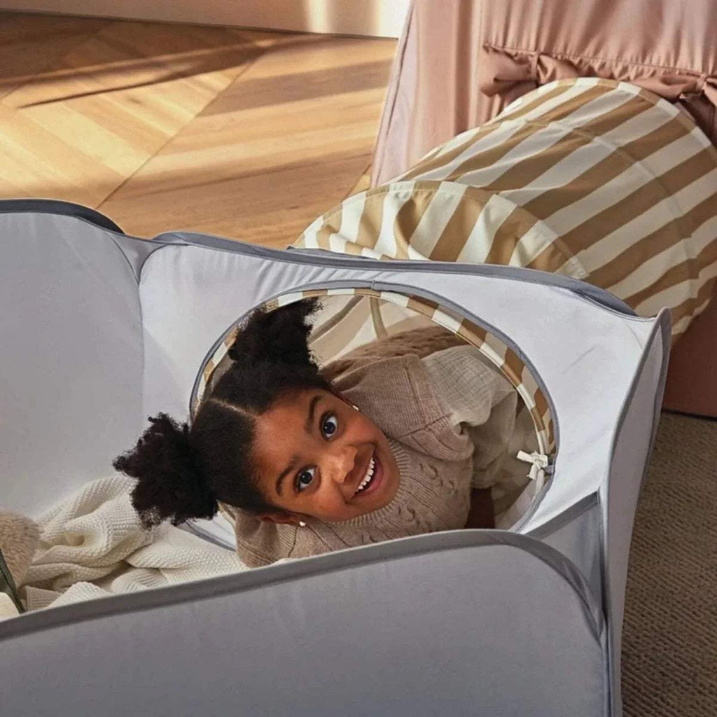 Child peeking from inside the light gray padded play tunnel within the set