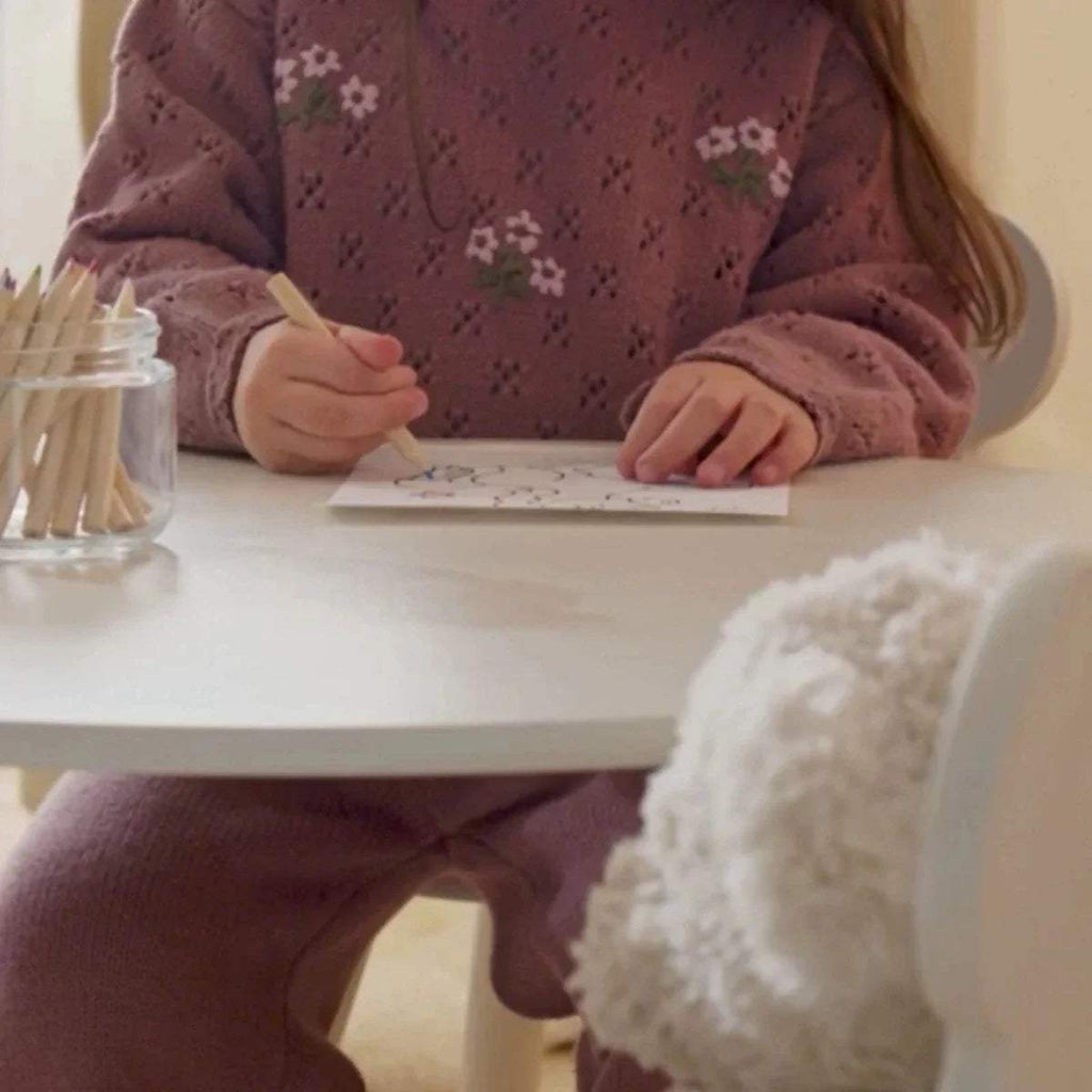 White kids play table with bear-back chair while a child writes and draws