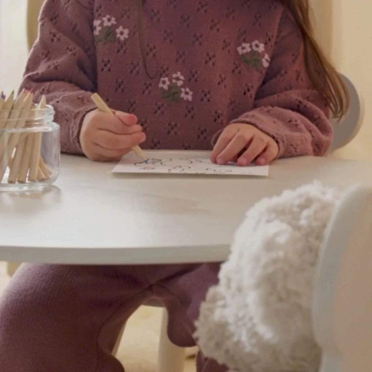White kids play table with bear-back chair while a child writes and draws