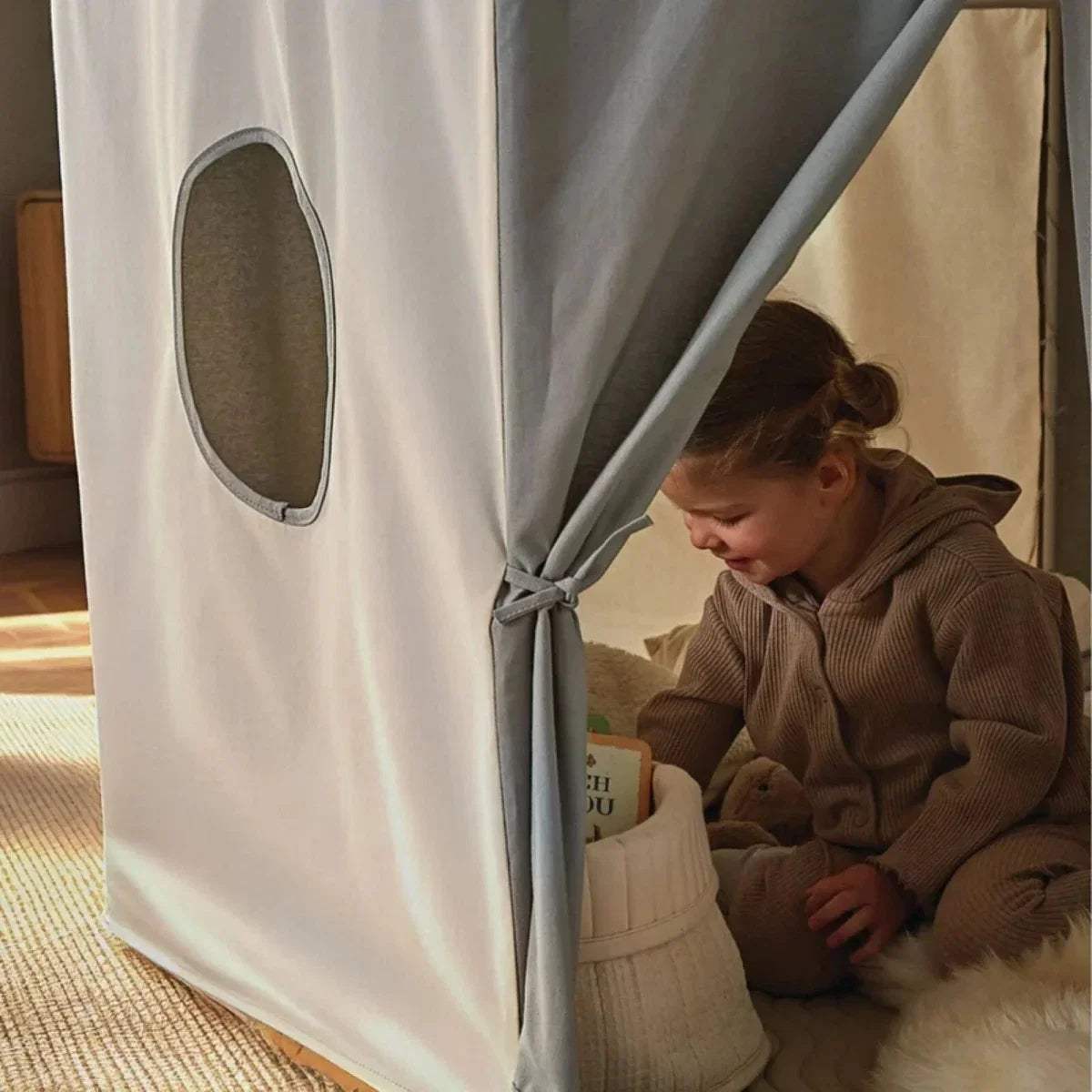 Play tent side door with oval window and tied-back flap; child sitting inside