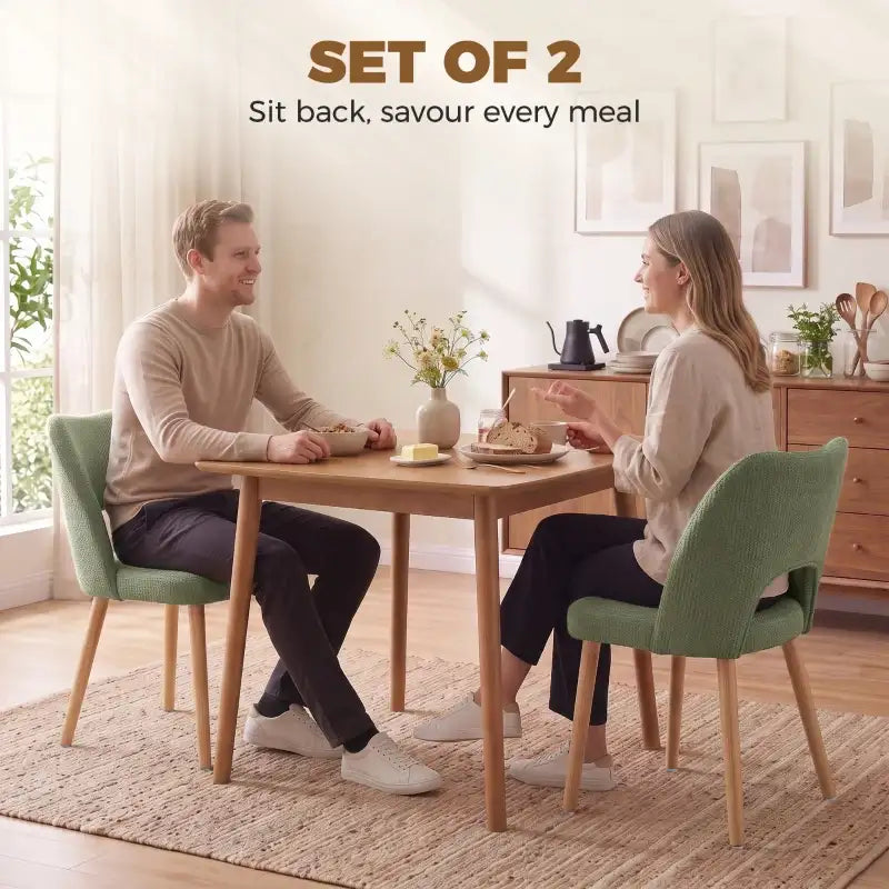 Set of 2 green upholstered dining chairs with curved backs and tapered light wood legs