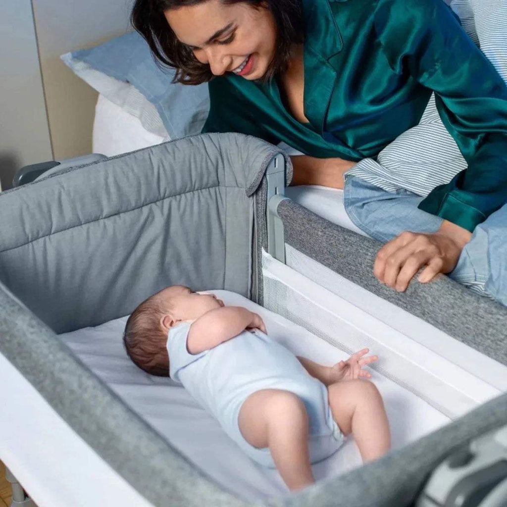 Dark gray bedside crib with padded rails and open side for baby