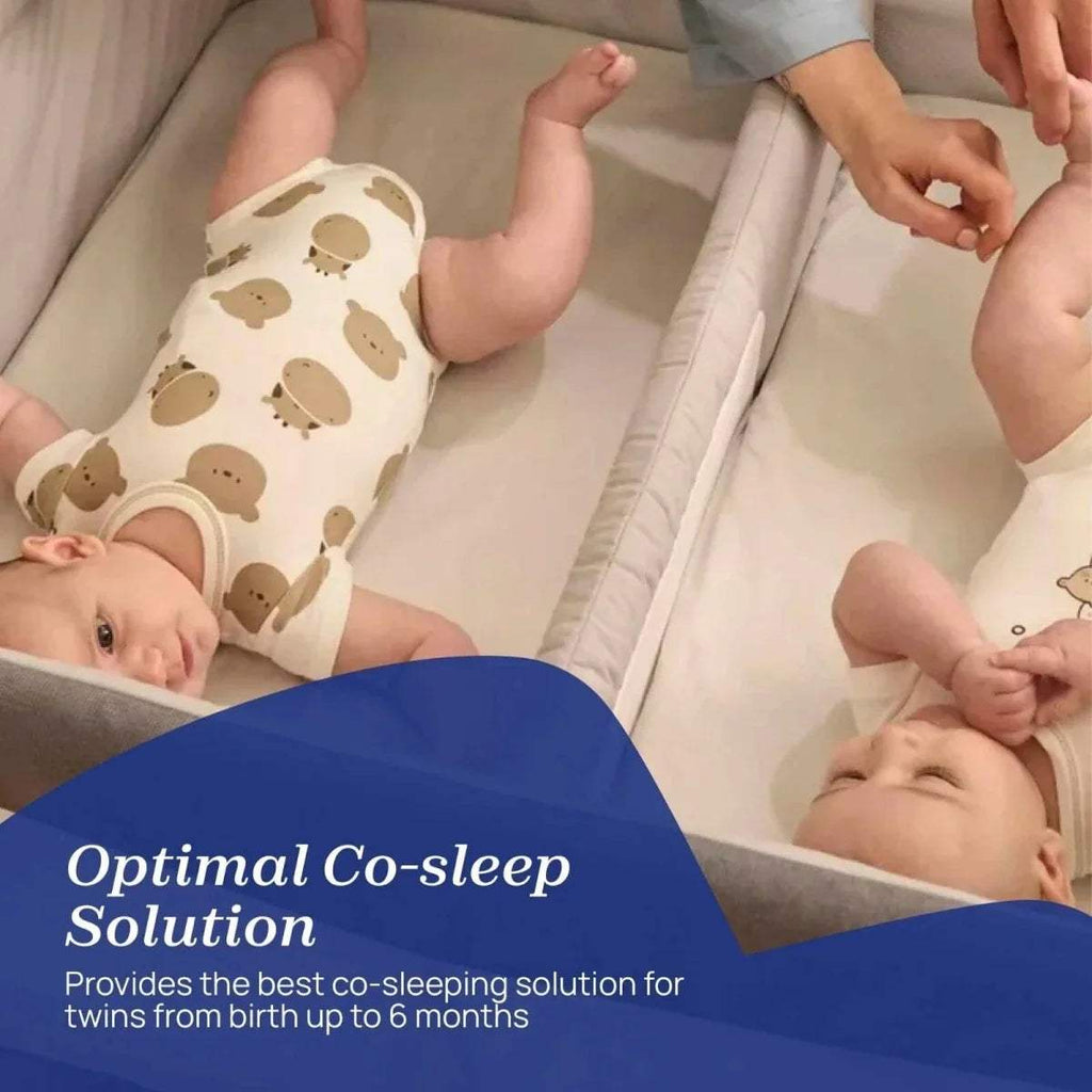 Twin bedside crib interior with two babies lying on a white mattress