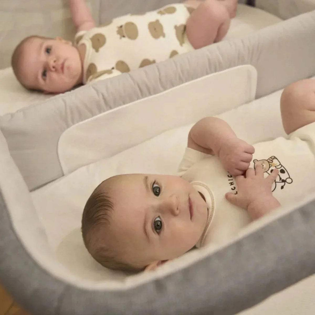 Magnet grey twin bedside crib close-up with padded base and two babies