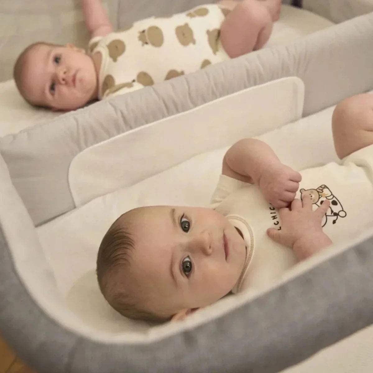 Magnet grey twin bedside crib close-up with padded base and two babies