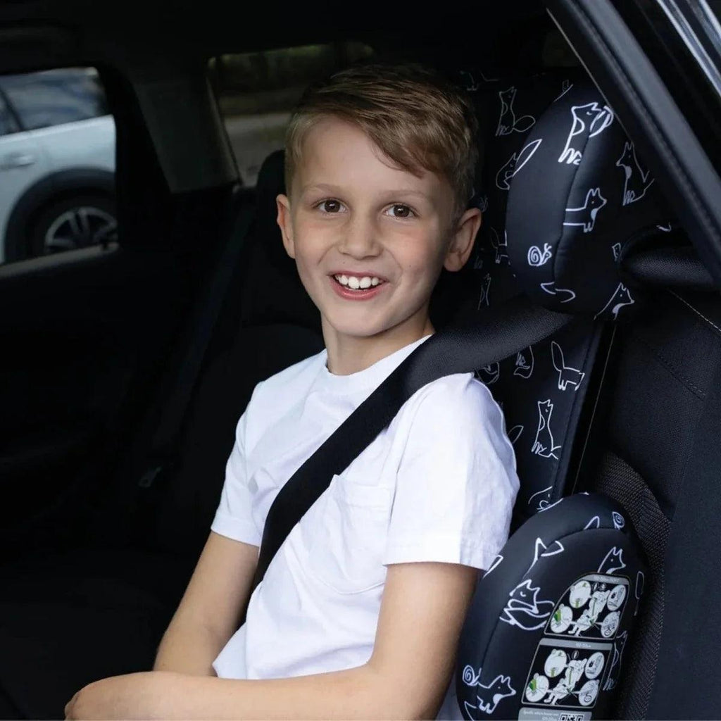 Child in Cosatto travel car seat, smiling, black patterned headrest and safety harness