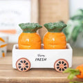 Orange carrot-shaped salt and pepper shakers with green tops in white wagon on wood