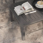 Outdoor coffee table with slatted dark top and thick legs, open book and cup