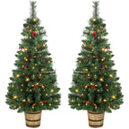 Two prelit green Christmas trees in pots with pinecones, berries, and warm white LED lights