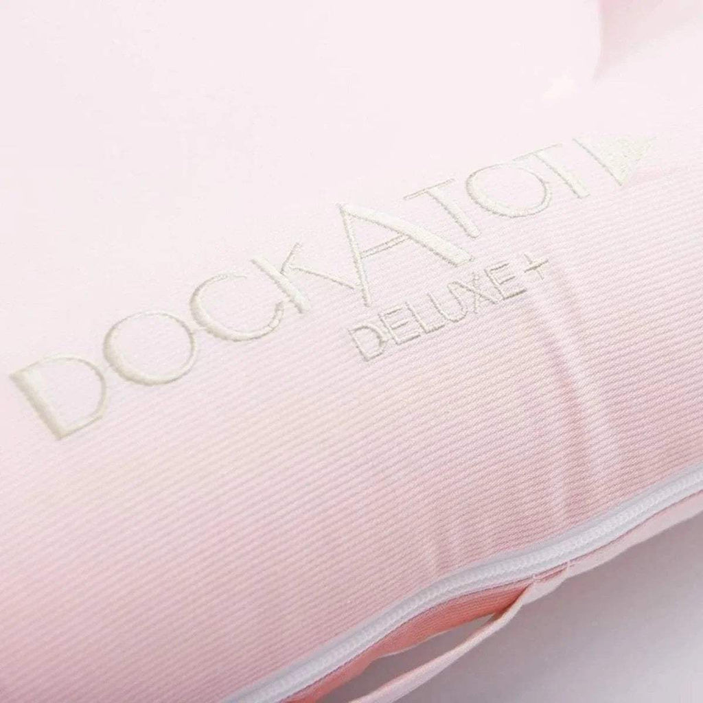DockATot Deluxe logo on pale pink plush fabric panel with light piping trim