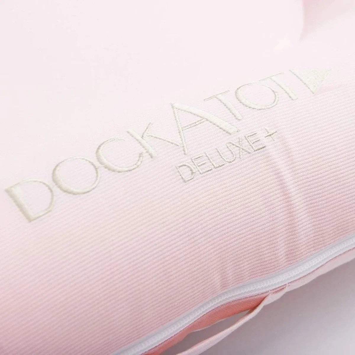 DockATot Deluxe logo on pale pink plush fabric panel with light piping trim