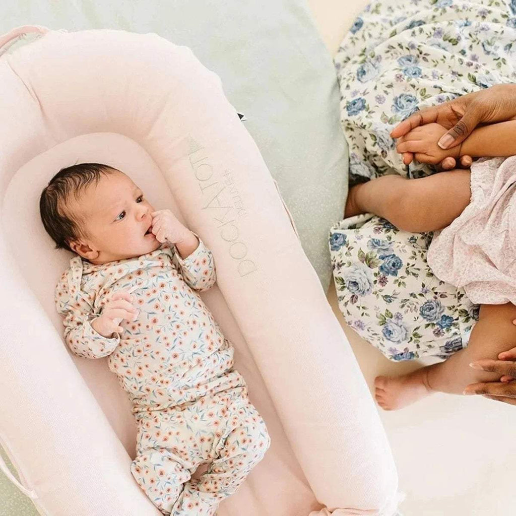 Pink infant dock with baby lying inside and DockATot logo on side bolster