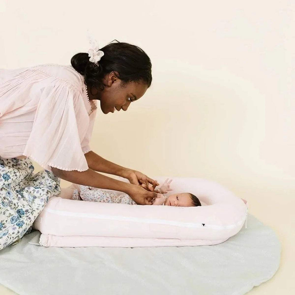 Pink infant dock on a bed with baby lying down; side bolster visible