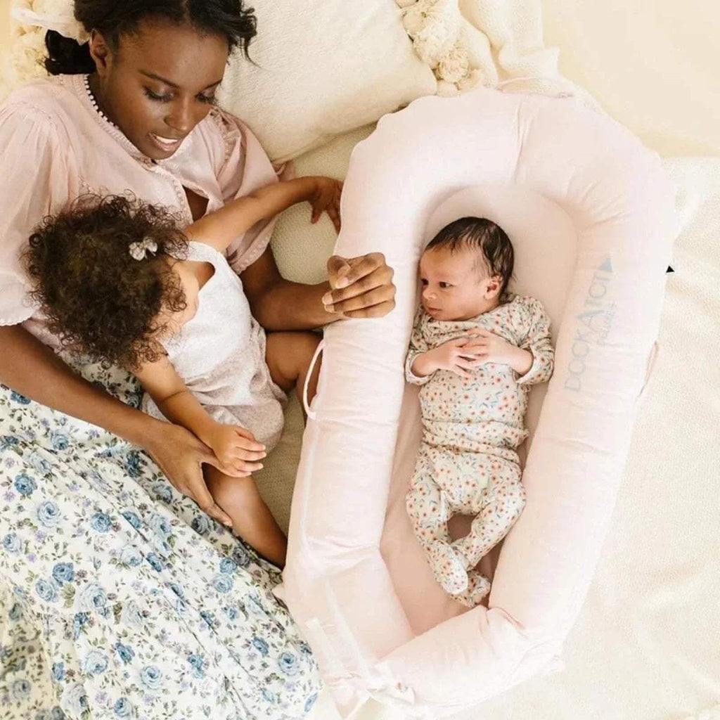 Pink infant dock with baby upright inside and DockATot logo on the side