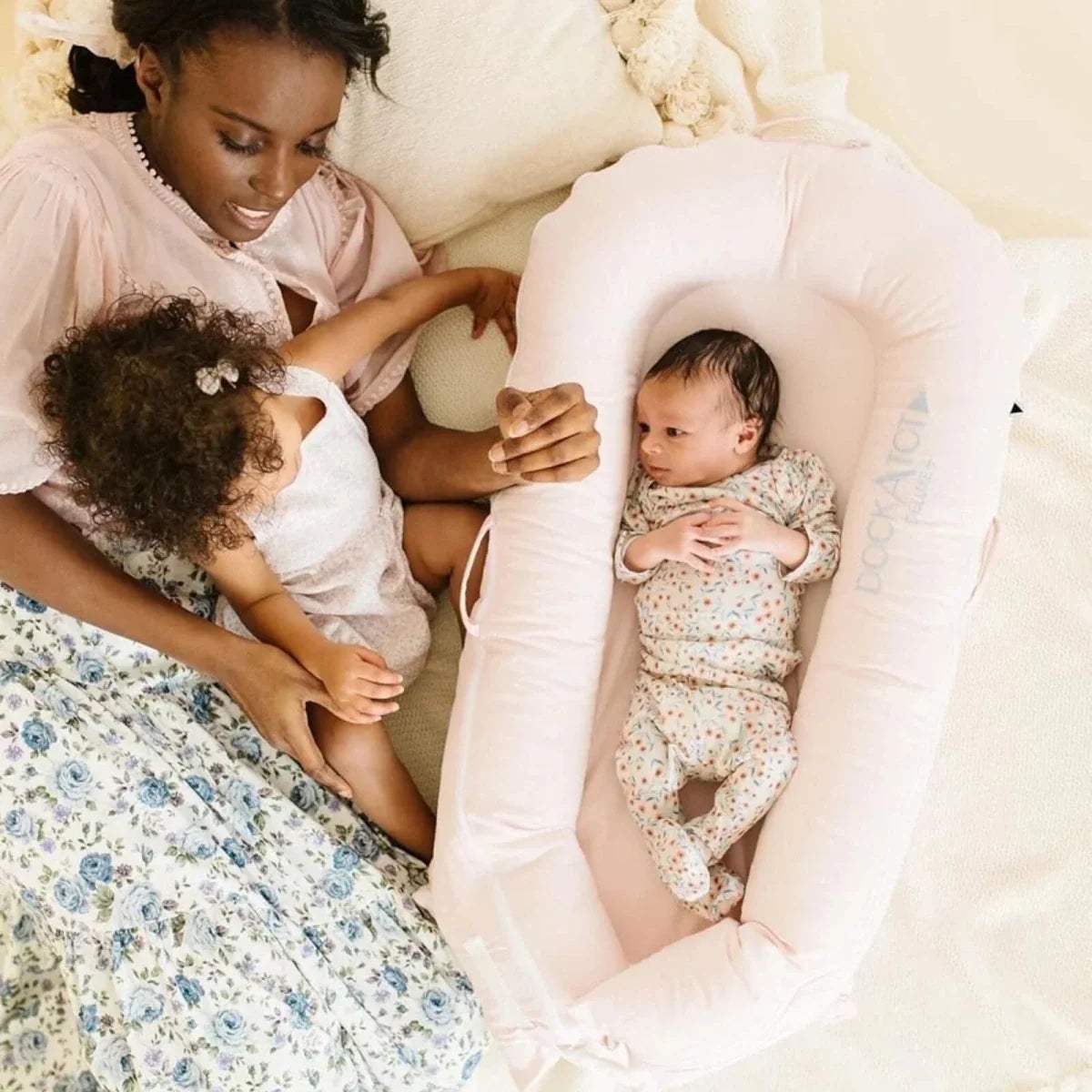 Pink infant dock with baby upright inside and DockATot logo on the side