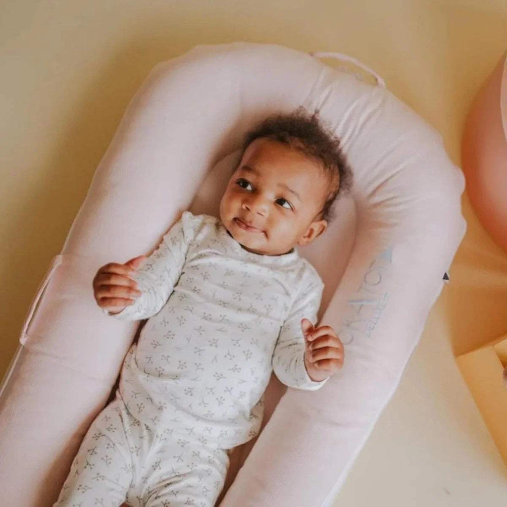 Pink infant dock with baby lying inside and DockATot logo visible on bolster