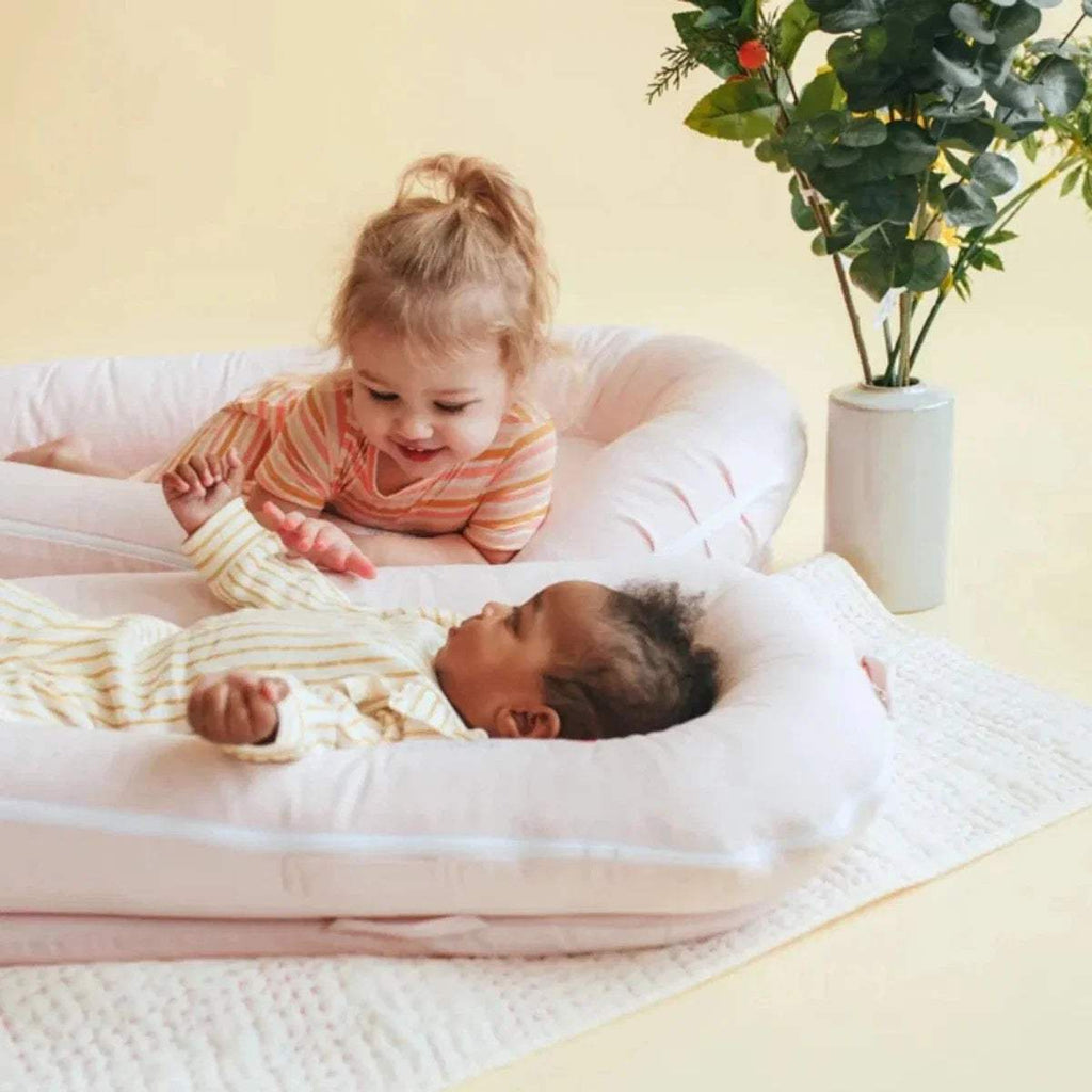 Cream DockATot Deluxe+ dock with striped cover, padded lounger with two children