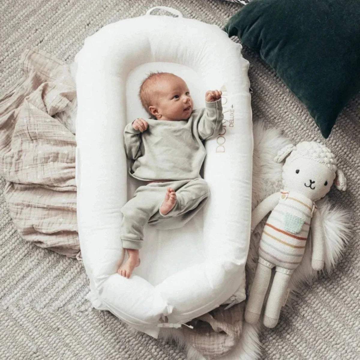 White baby dock on a blanket, shown with infant and plush toy