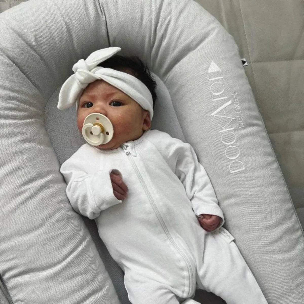 Baby lying in light gray padded DockATot dock with embossed side logo
