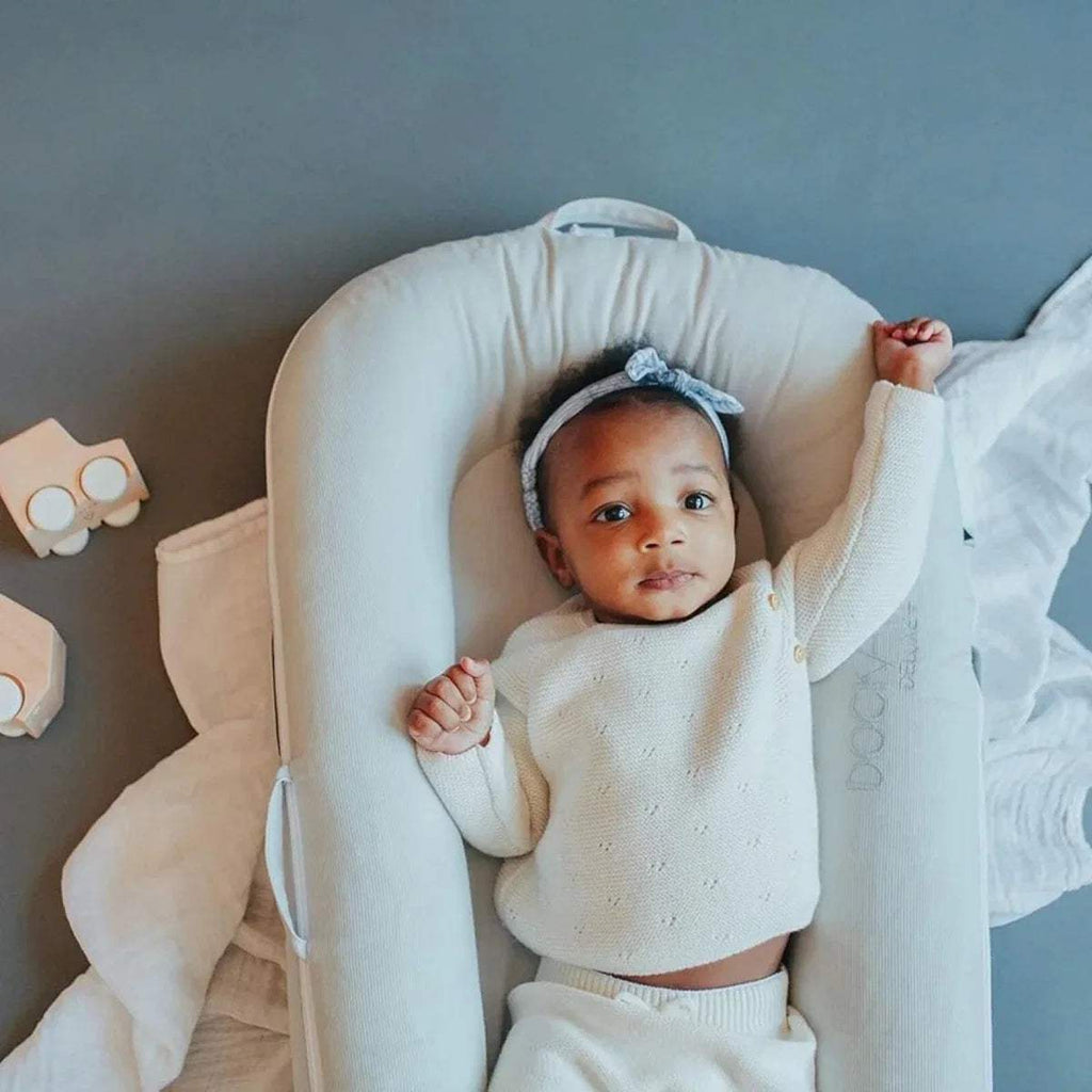Baby resting in light gray DockATot dock with side bolster visible