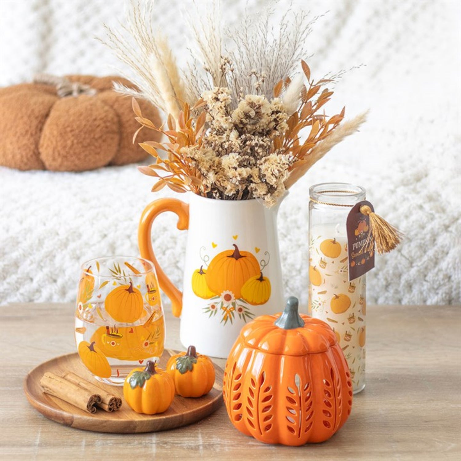 Decorative items including a mug with pumpkins, a candle, and small pumpkins on a wooden surface.