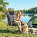 Black padded reclining folding camping chair with wide armrests by a lakeside tent