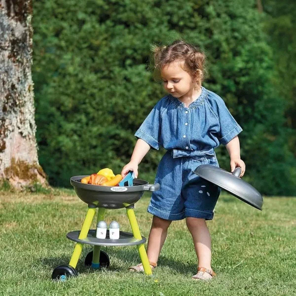 Kids toy BBQ grill with open top; child holds spatula at dark lid on lime stand