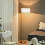 Standing floor lamp with gold pole and white drum shade in warm light