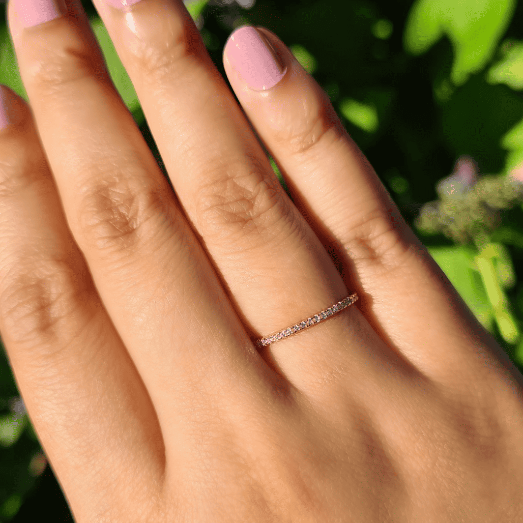 Thin rose gold eternity ring with small stones on a hand