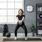 Gray and yellow 4 kg kettlebell held for strength training on a floor mat