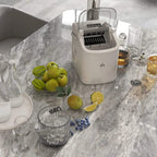 White countertop ice maker with open lid on marble-style counter and ice scoop accessories