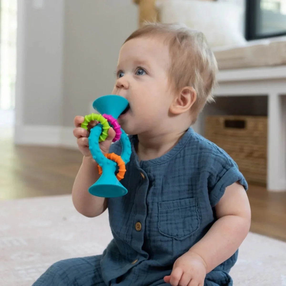 Baby holding a teal loop teether with colorful squiggle links