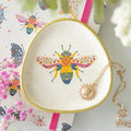 Round ceramic trinket dish with gold rim, speckled white finish, colorful bee graphic
