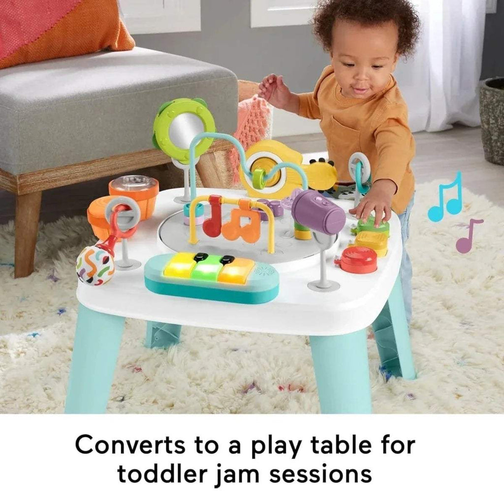 Baby reaching for toys on a white activity centre table with teal legs and push buttons
