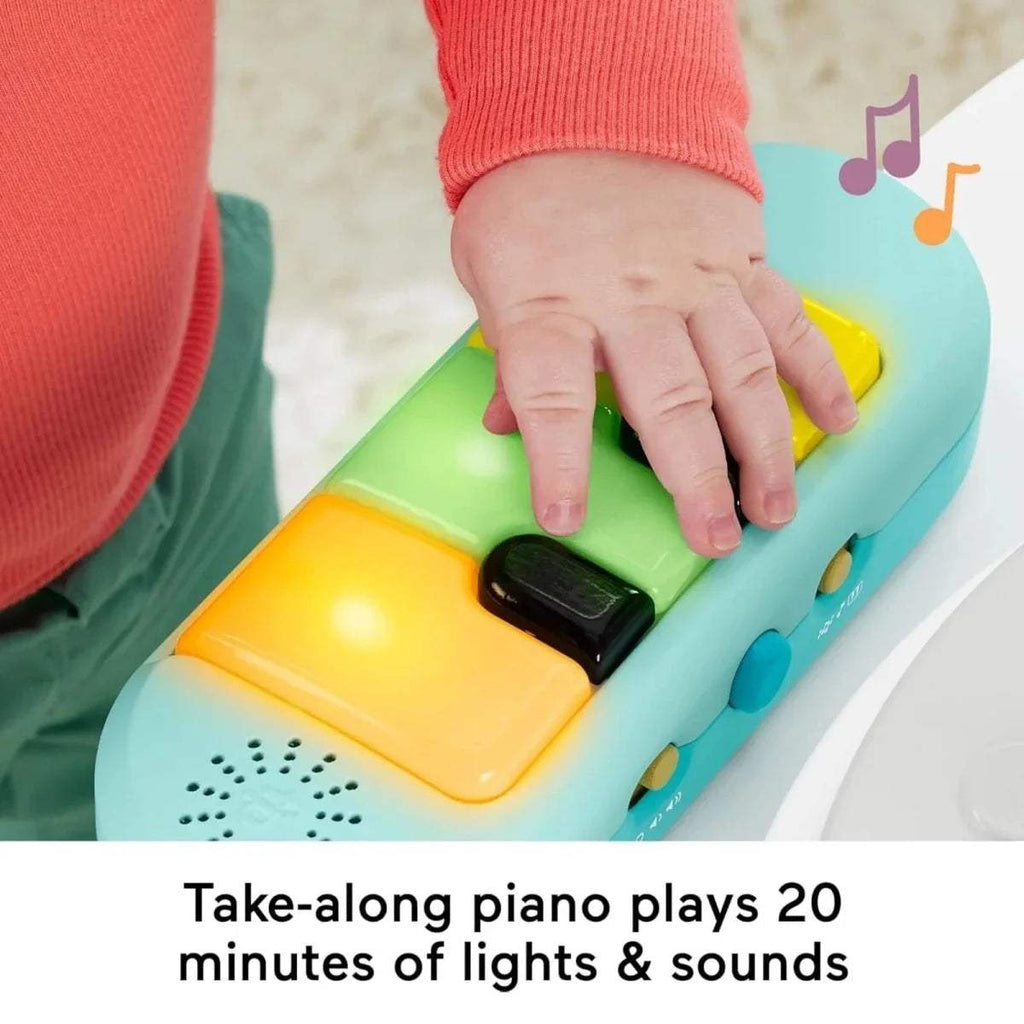 Close-up of a baby hand pressing a yellow button panel on a teal-and-white toy piano