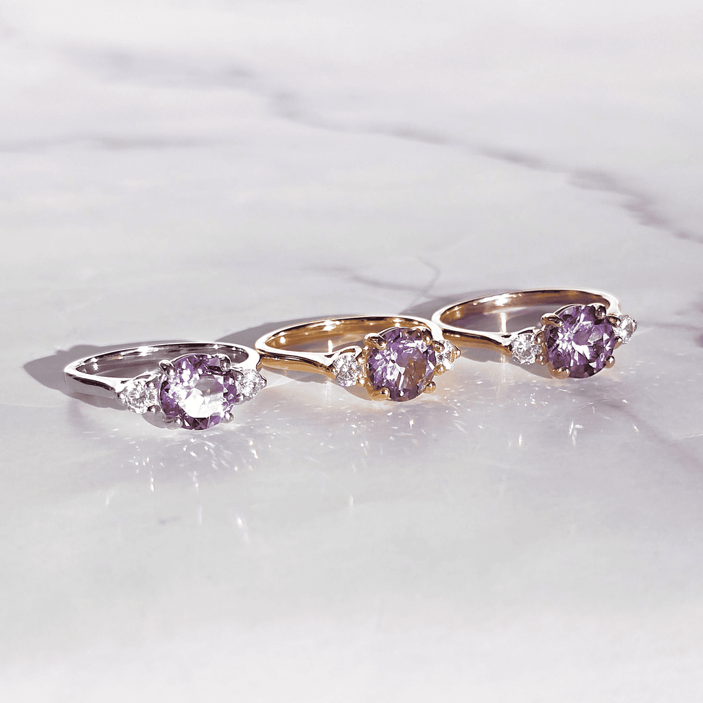 Three oval lavender-stone rings in gold and silver tones on light surface