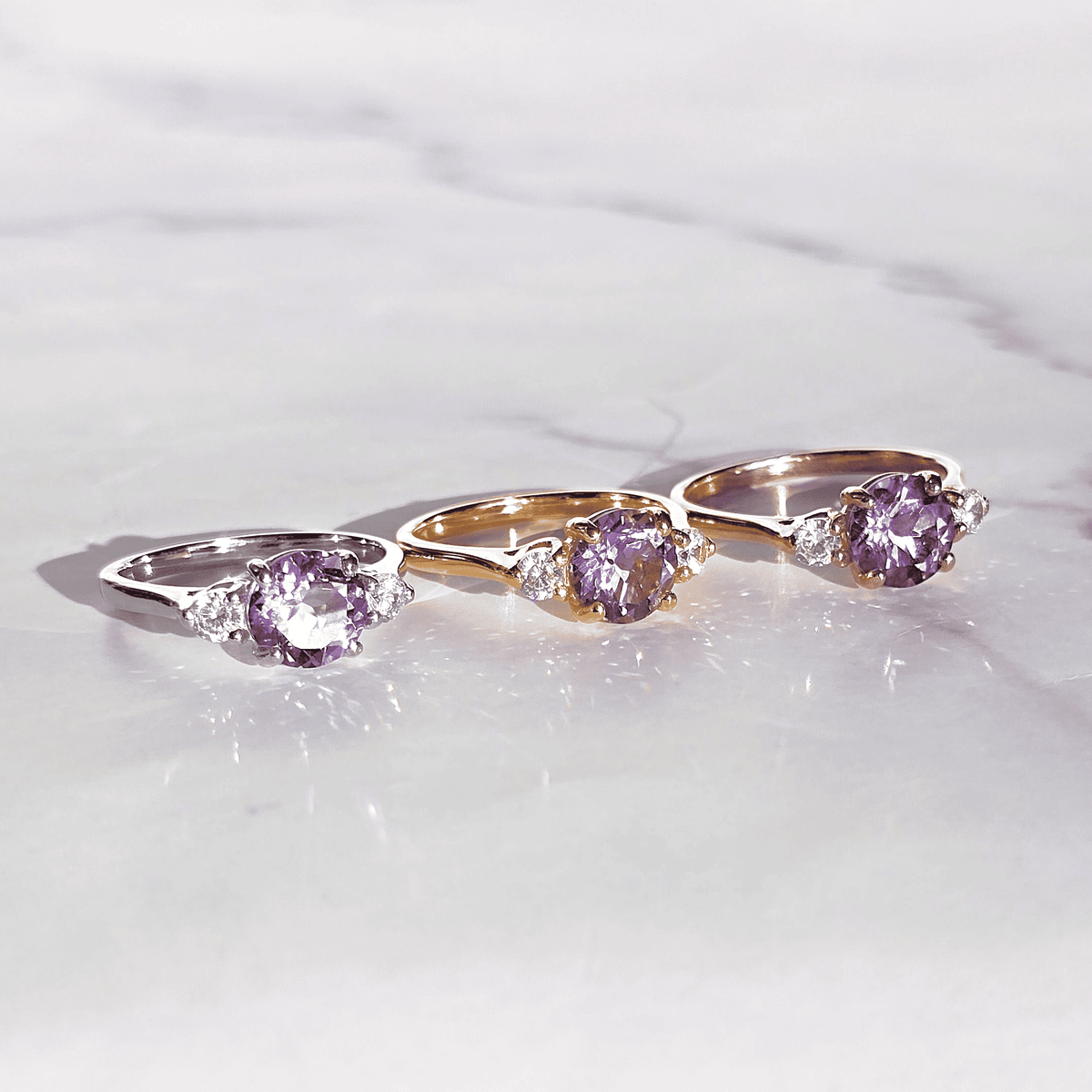 Three oval lavender-stone rings in gold and silver tones on light surface