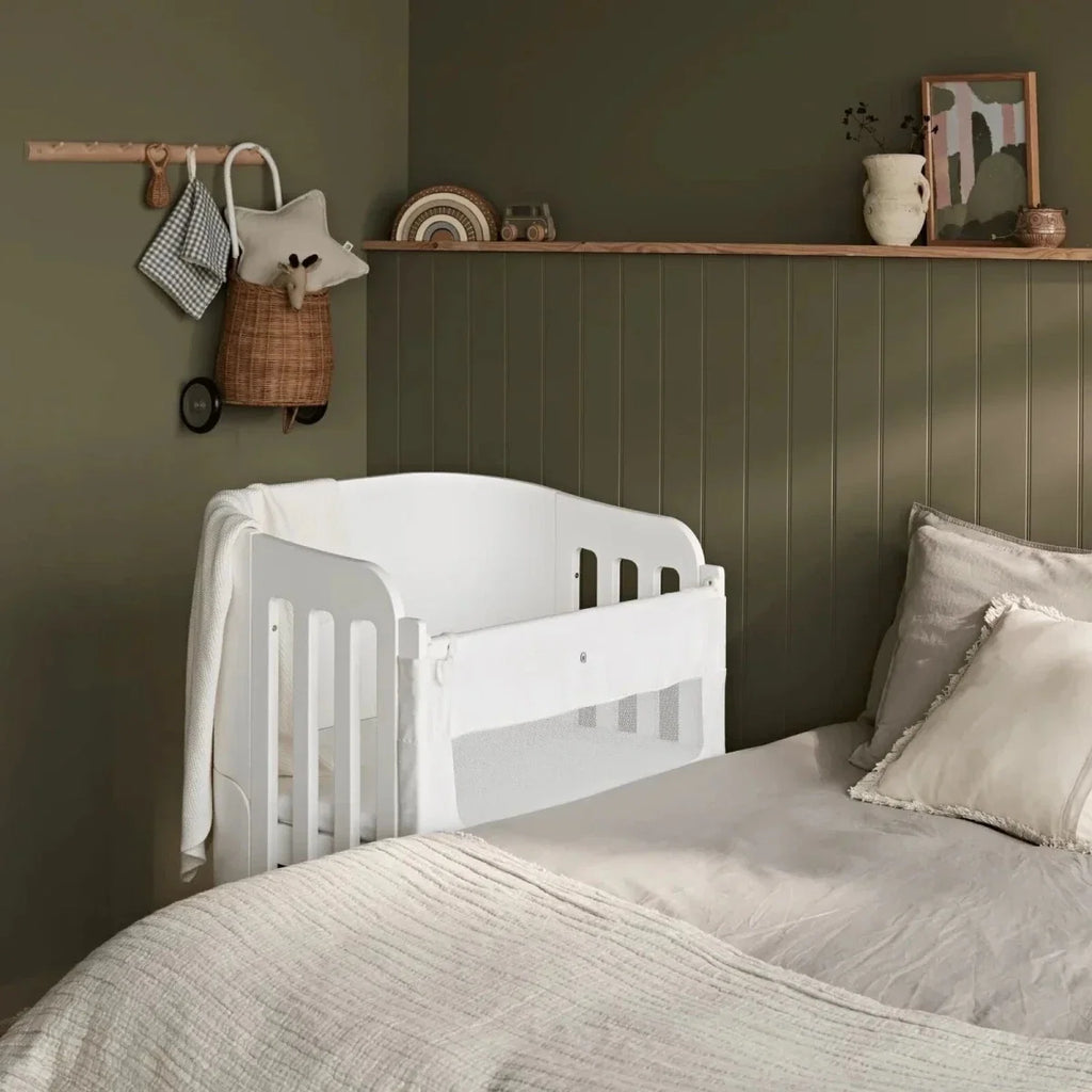 White baby cot bed with slatted end panels, rounded corners, and natural wood legs