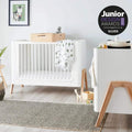 Convertible cot bed with white frame, vertical slats, light wood legs, and safety rail ends