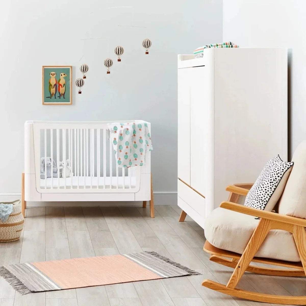 Convertible cot bed with white sides and light wood feet, empty crib position with blanket drape