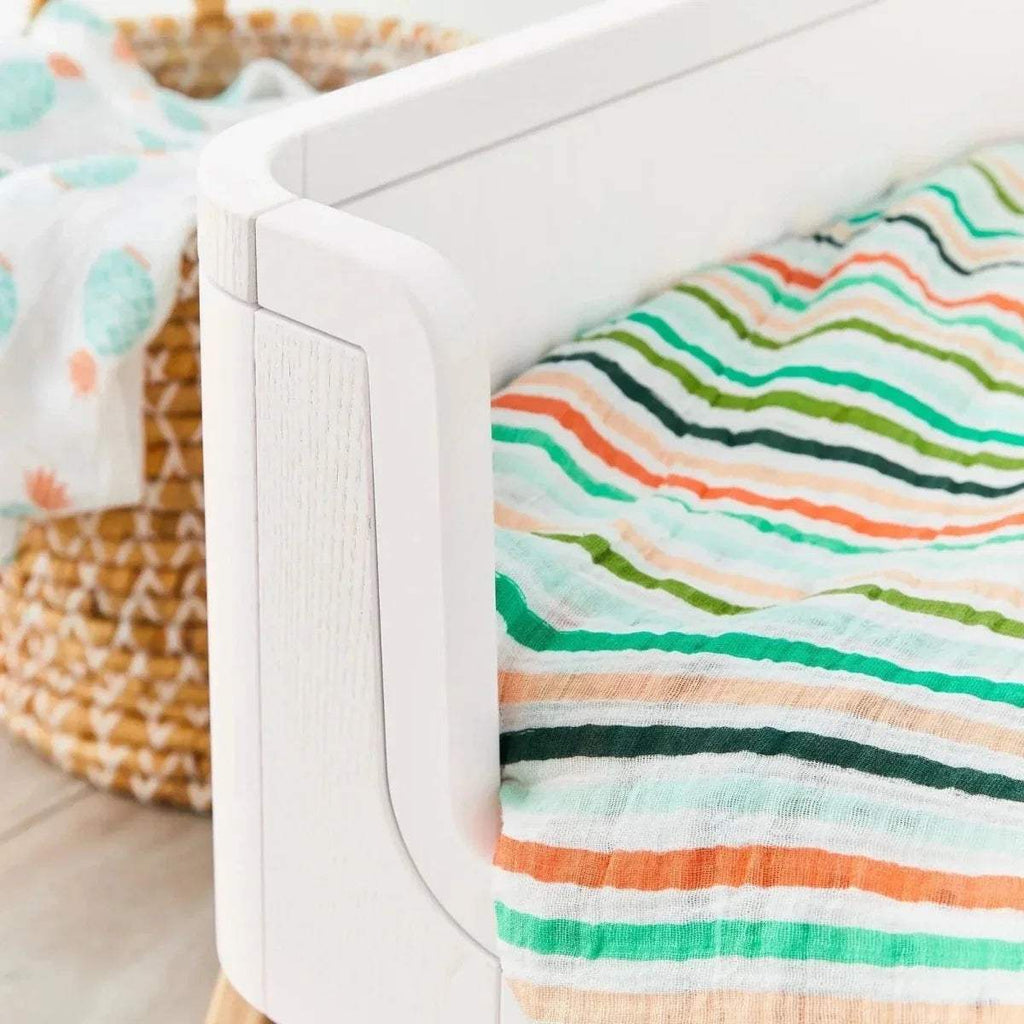 Close-up of white cot bed corner post with rounded edge and attached fabric bedding