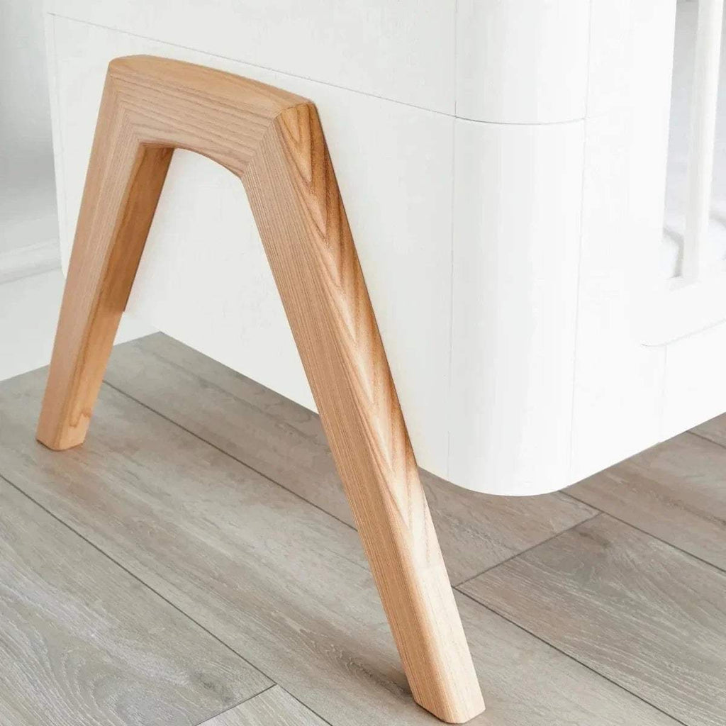 Light wood cot bed leg with angled support, attached to a white panel base