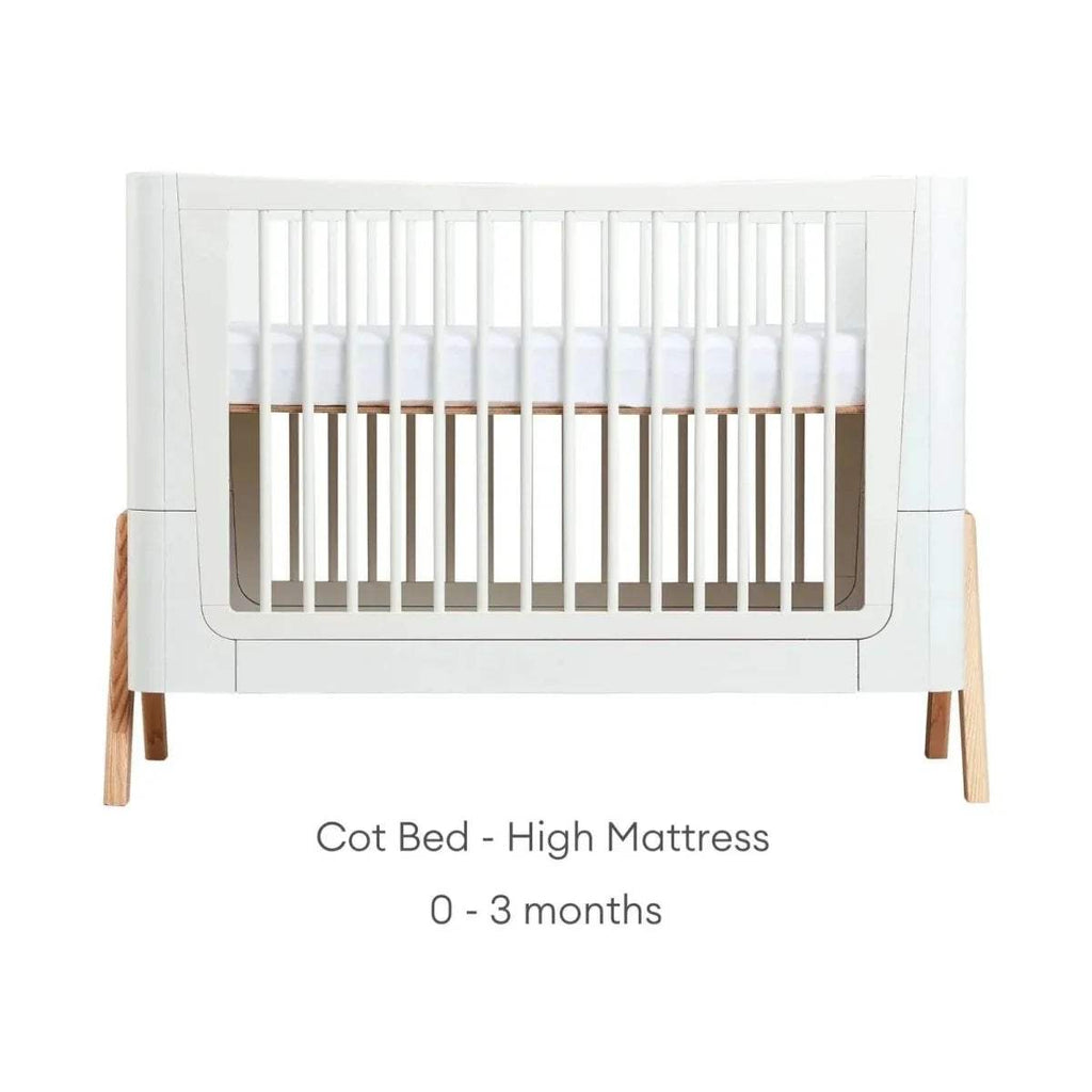 Cot bed frame in white with light wood legs, shown in high mattress setup position