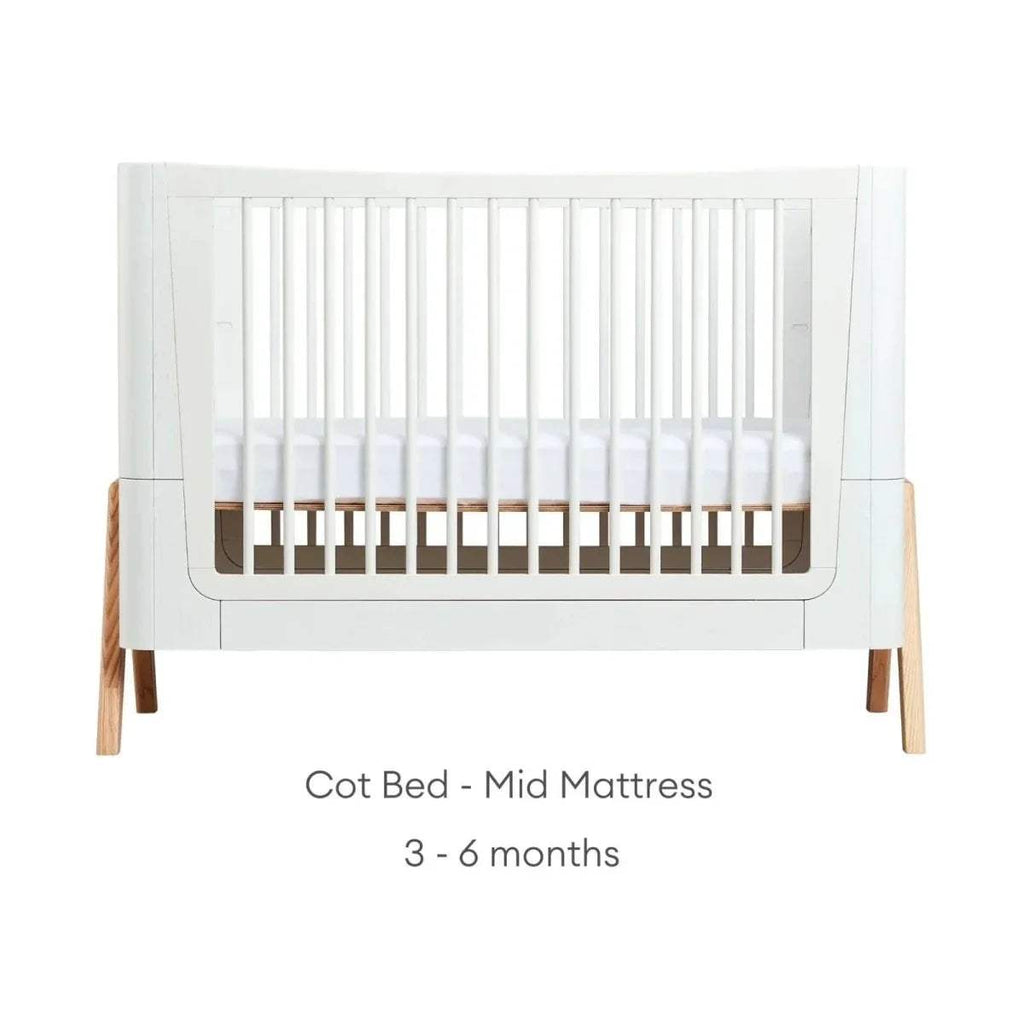 Cot bed frame in white with light wood legs, shown in mid mattress setup position