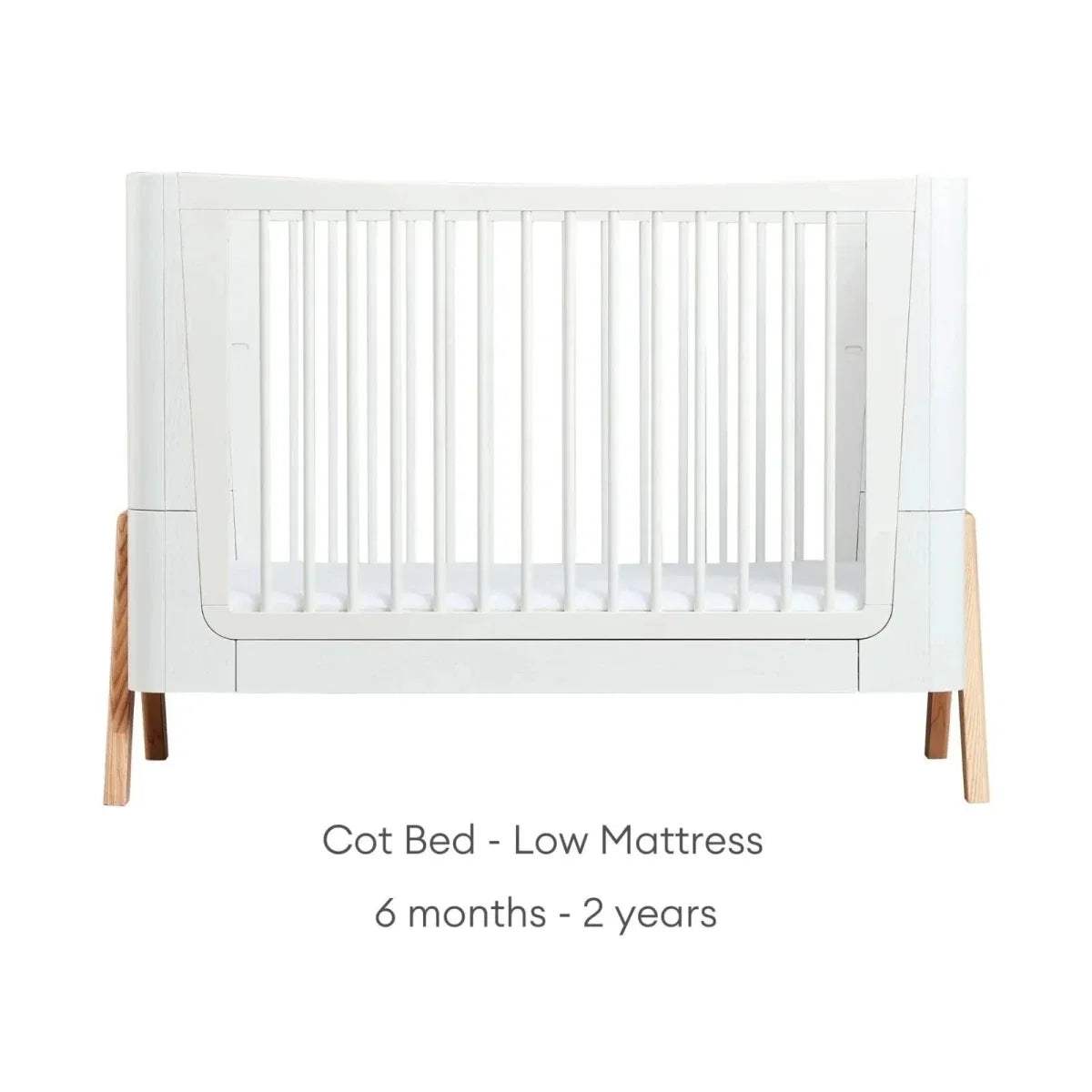 Convertible baby cot bed with white slatted sides and natural wood legs
