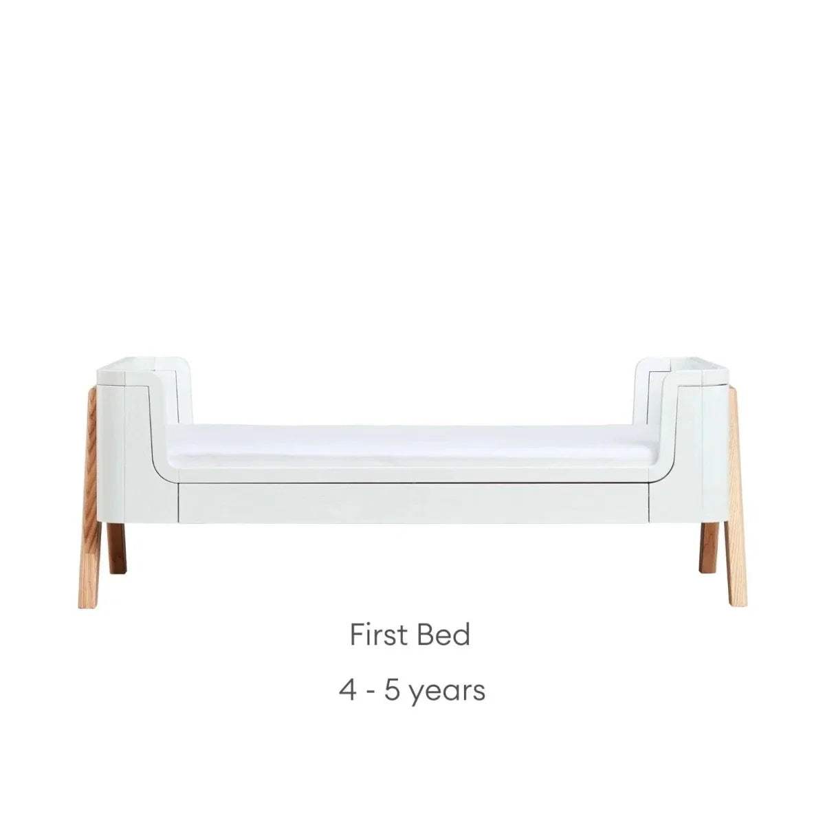 Convertible baby bed in first-bed mode with white frame and natural wood legs