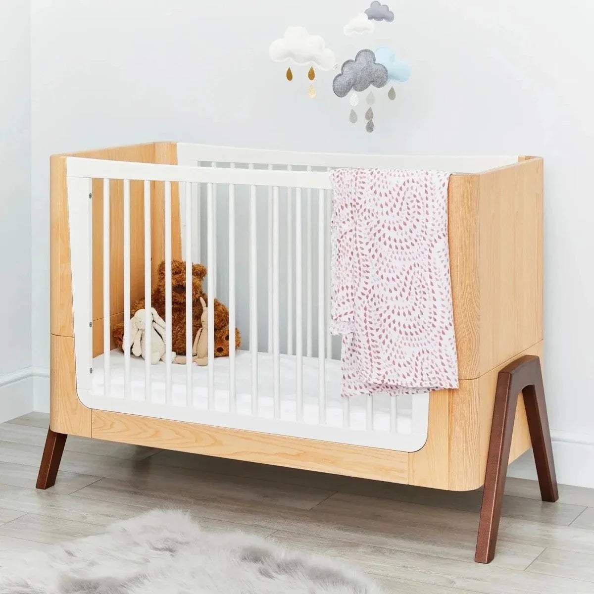 Convertible baby cot bed with white slats, natural wood frame, and draped cloth