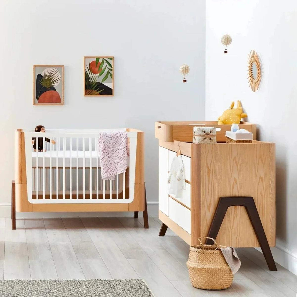 Convertible baby cot bed with white slatted sides, natural wood frame, dark legs