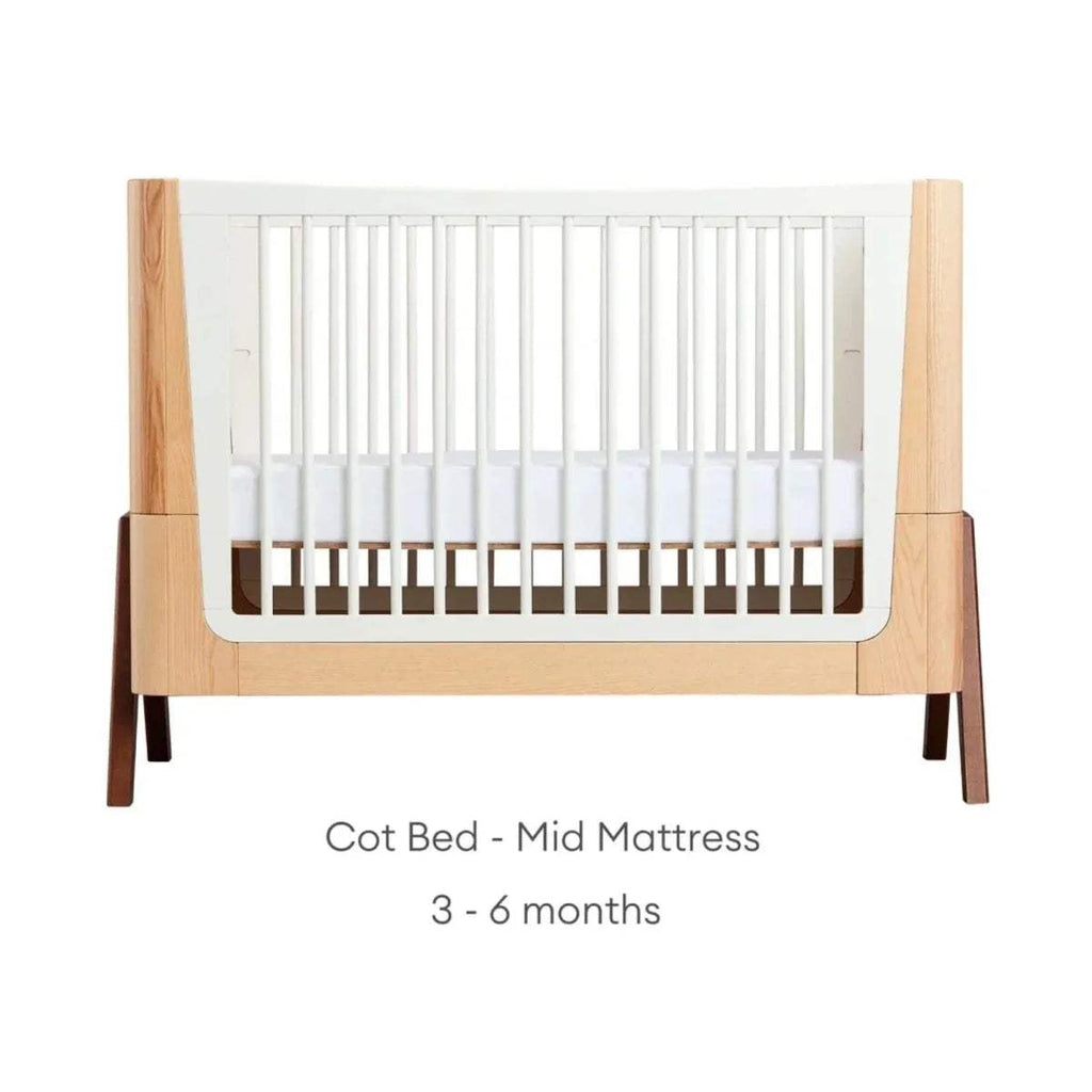 Convertible cot bed with natural wood frame and white slat sides; mid-height white mattress